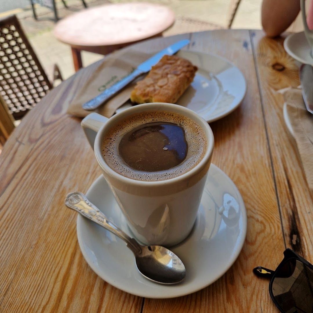 A black coffee in a white cup and a slice of cake on a wooden café table